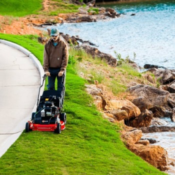 man cutting grass with an exmark push mower near water's edge